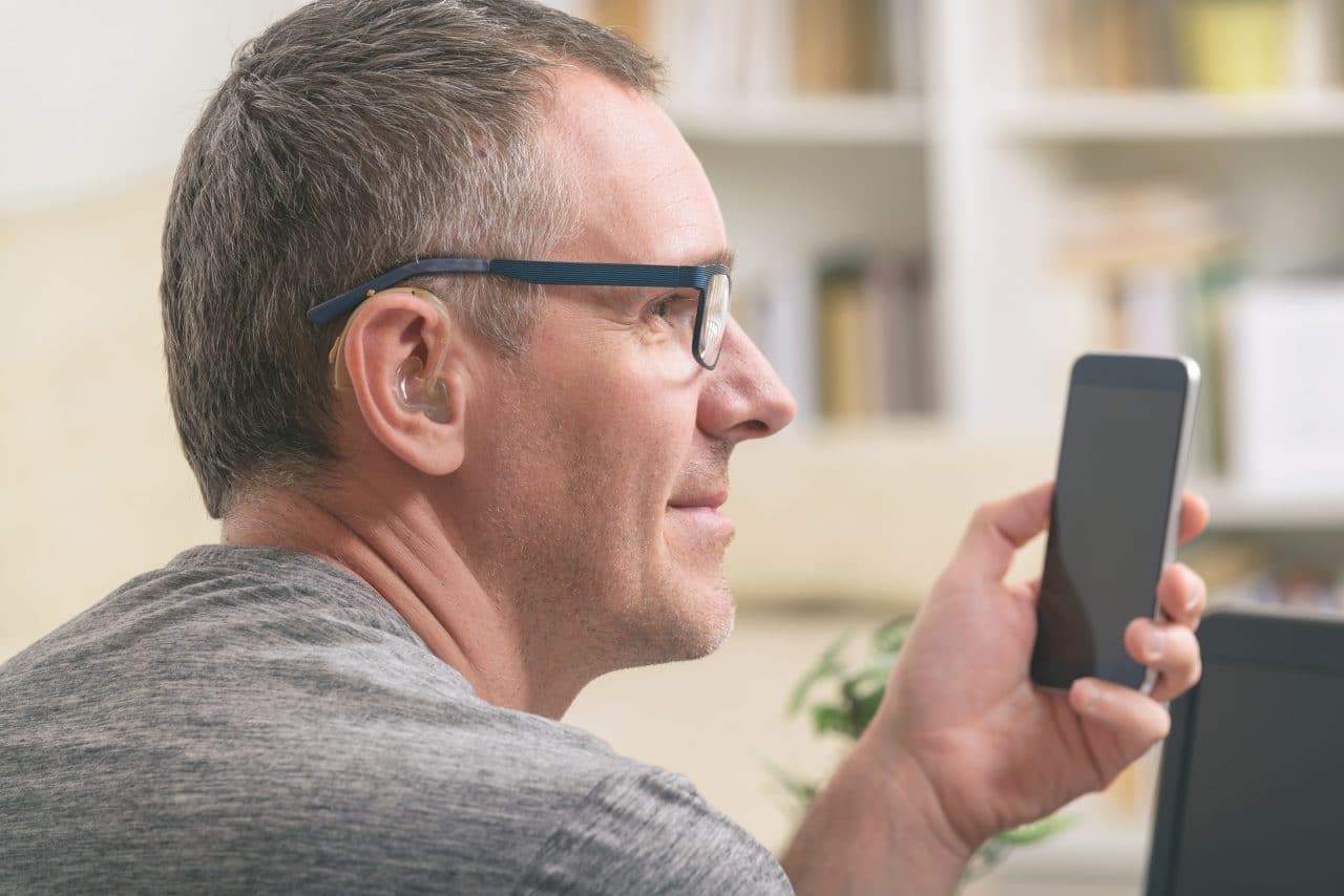 Man with a hearing aid uses his smartphone.