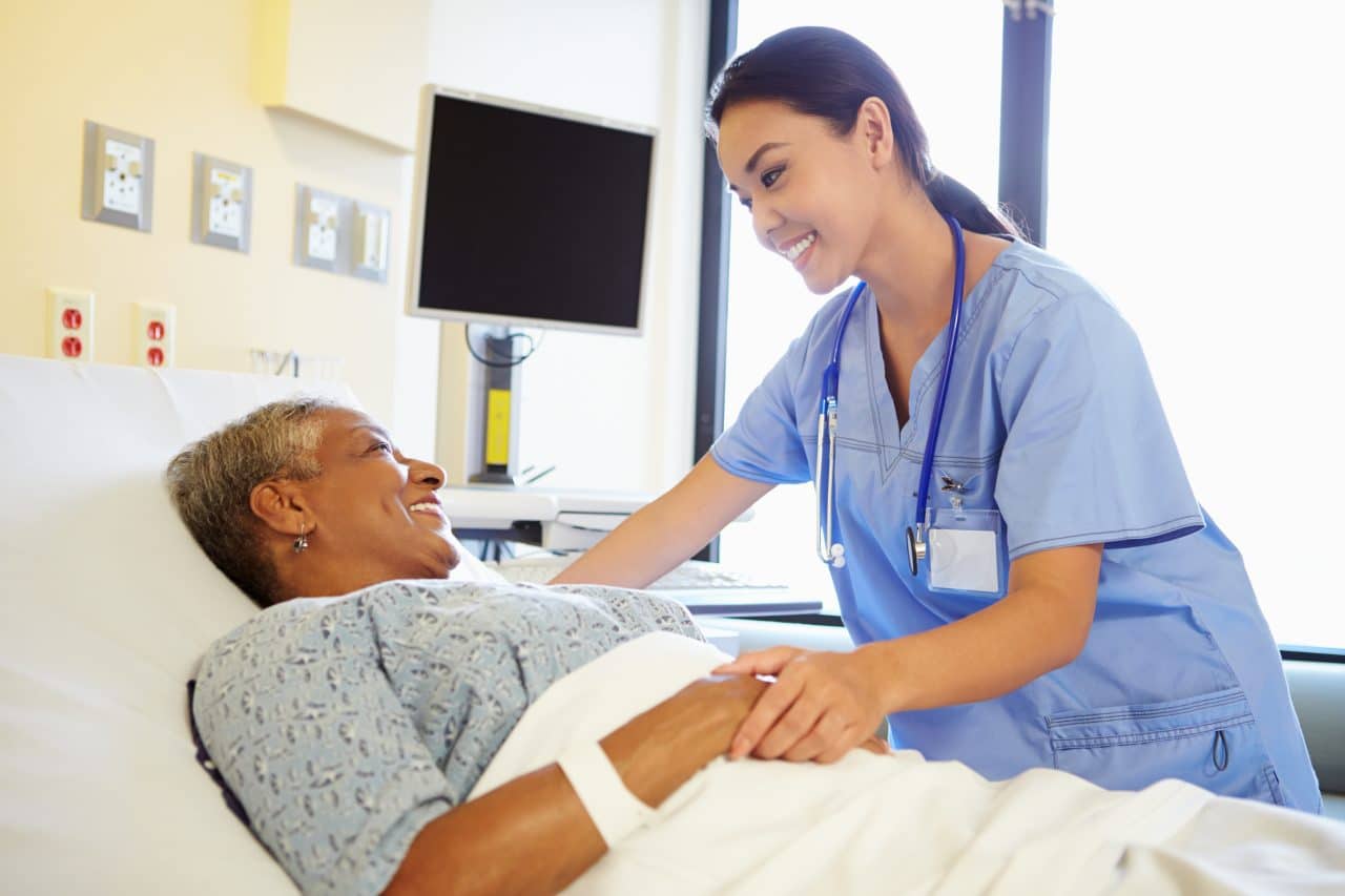 Nurse chats with patient in hospital room.