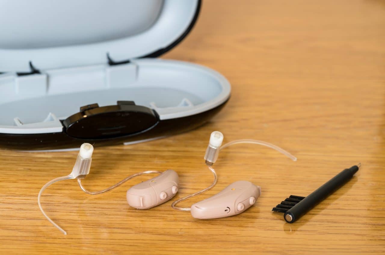 Close up of hearing aids and a cleaning brush for proper care.