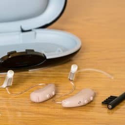 Close up of hearing aids and a cleaning brush for proper care.