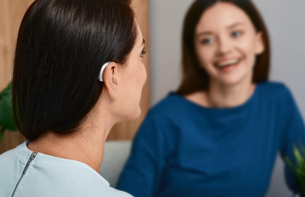 Woman with a hearing aid talking with her friend at home.