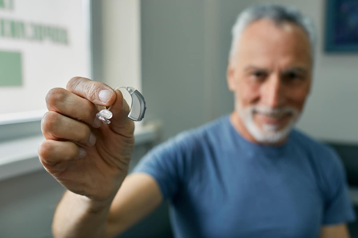 Senior man holding up a behind-the-ear (BTE) hearing aid.