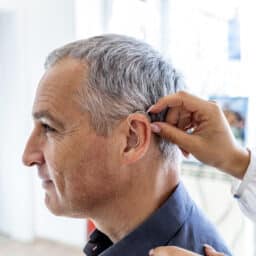 Photo of an audiologist inserting hearing aid in man's ear