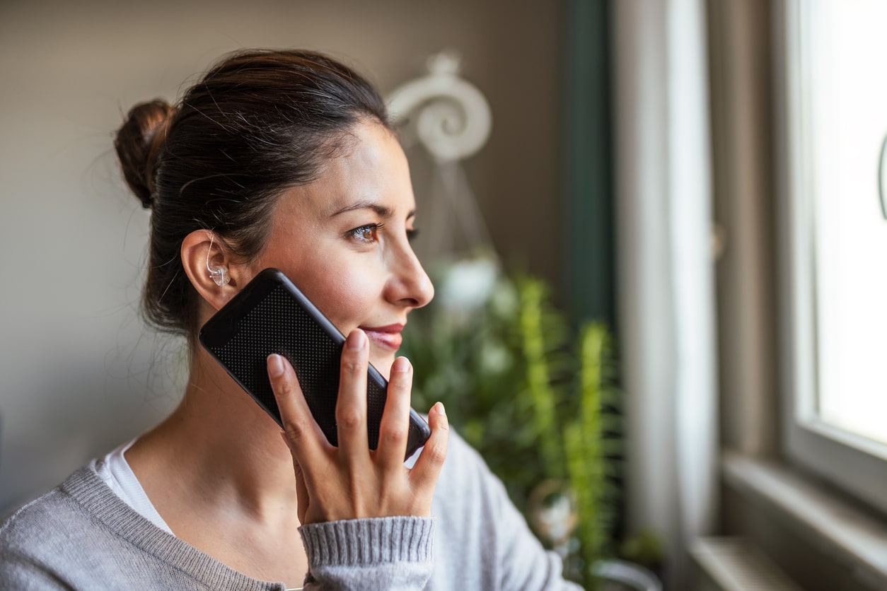 Woman wearing a hearing aid holder a phone next to her ear