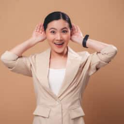 Happy woman holding her hands to her ears on a tan background